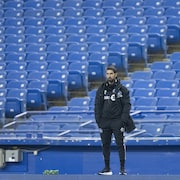 Un homme se tient debout, seul, devant les gradins vides d'un stade.