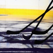 On aperçoit les contours de plusieurs bâtons de hockey sur une patinoire.