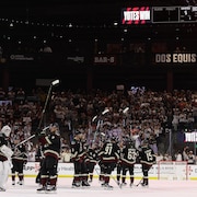 Réunis au centre de la patinoire, des joueurs de hockey lèvent leur bâton en direction des gradins.