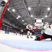 Depuis l'intérieur du filet, gros plan d'une rondelle qui entre dans un filet pendant un match de hockey féminin