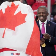 L'homme se prépare à remettre une médaille d'or à un joueur qui est enveloppé d'un drapeau canadien.