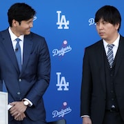 Deux hommes en veston se tiennent debout devant le logo des Dodgers.
