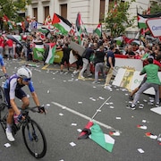 Des manifestants sont contenus par des gardiens de sécurité pendant que des cyclistes passent tout près.