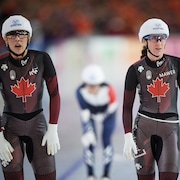 Deux patineuses de vitesse sont côte à côte sur une patinoire, avec sur leur tête lunettes et casque de protection.
