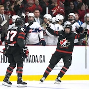 Deux joueuses de hockey se regardent en souriant. Les joueuses de l'équipe adverse sont sur le banc à l'arrière et les observent.