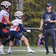 Un entraîneur de football regarde deux joueurs effectuer un exercice sur le terrain.