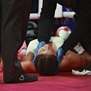 Des personnes sont au chevet d'une boxeuse couchée dans le ring.
