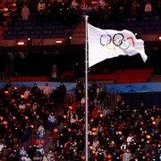 Un drapeau affichant les cinq anneaux olympiques flotte au vent.