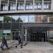 Trois policiers marchent près de la porte d'entrée d'un édifice à bureaux.