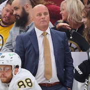 Un homme qui porte un complet se tient debout derrière le banc d'une équipe de hockey.