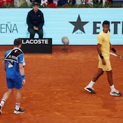 Un joueur de tennis en regarde un autre, qui marche avec une serviette sur l'épaule.