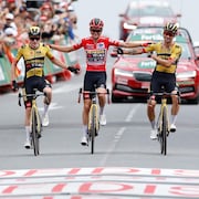 Trois cyclistes souriants se tiennent par les bras et passent la ligne d'arrivée ensemble. 