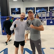 Deux hommes posent pour la caméra dans un centre d'entraînement d'arts martiaux mixtes.