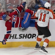 Un joueur de hockey est en train de tomber sur la glace alors qu'un adversaire vient de le plaquer contre la bande.