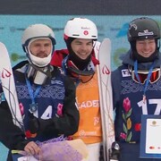 Mikaël Kingsbury, au centre, pose pour la photo avec les deux autres skieurs sur le podium. Tous les trois sont souriants. 
