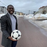 Homme avec manteau tenant un ballon de soccer en souriant.