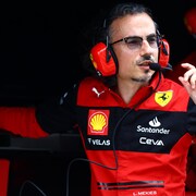Un homme à lunettes, avec un casque d'écoute sur la tête et une chemise de Ferrari, parle dans un micro.