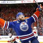 Un joueur de hockey en bleu lève les bras en triomphe.