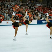 Des patineuses de l'équipe des Suprêmes se tiennent un pied derrière la tête pendant une compétition. 