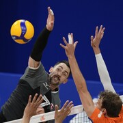 Timothy Maar frappe le ballon au-dessus du filet, contré par des adversaires.