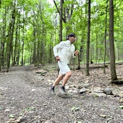 Un homme, v&ecirc;tu de v&ecirc;tements blancs et d'une casquette noire, court sur un sentier en for&ecirc;t.