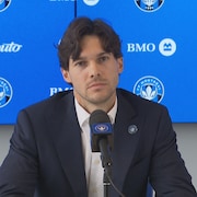 Il est assis derri&egrave;re un micro.