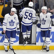 Un joueur de hockey sort de la glace, deux autres de la même équipe attendent sur la glace et semblent déçus.