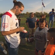 Marc-Antoine Dequoy signe un autographe sur la casquette d'un jeune footballeur lors d'une activité à Kahnawake.