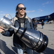 Un jeune homme tient la coupe Grey sur la piste d'atterrissage d'un aéroport.