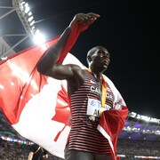 Le Canadien Marco Arop sourit, la médaille au cou, le drapeau unifolié sur ses épaules, après sa course. 