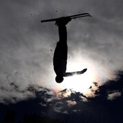 Une skieuse acrobatique à l'envers dans les airs.