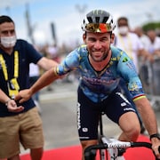 Un cycliste très souriant, de face, lâche la main d'un membre de son équipe et commence à rouler.