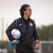 Un entraîneur de soccer tient un ballon sous son bras droit.