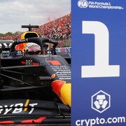 Un pilote de F1 place sa monoplace derrière un panneau qui désigne le gagnant. On voit le chiffre 1 écrit dessus.