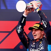 Un pilote de F1 soulève un trophée à deux mains et réagit, visiblement très heureux.