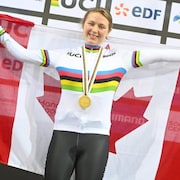 La paracycliste sourit, médaille d'or au cou, en tenant le drapeau canadien
