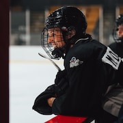 L'hockeyeuse est debout au banc et regarde l'action sur la patinoire.