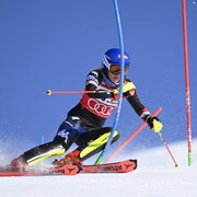 Une skieuse casquée passe à droite d'une porte pendant une compétition disputée sous un ciel sans nuage.