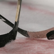 Deux bâtons de hockey et une rondelle, lors d'une mise en jeu. 