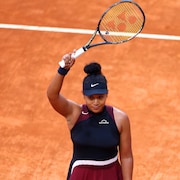 Une joueuse de tennis lève le bras droit, qui tient sa raquette, au dessus de sa tête. 