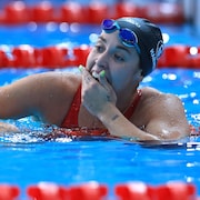 La nageuse, dans la piscine, couvre son sourire avec sa main.
