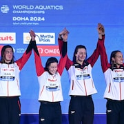 Rebecca Smith, Sarah Fournier, Katerine Savard and Taylor Ruck, mains dans la main, lèvent les bras dans les airs en célébrant leur médaille de bronze.