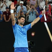 Un joueur de tennis lève les bras, sa raquette dans la main gauche, pour remercier la foule qui l'applaudit. 