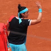 Une joueuse de tennis, de dos, salue la foule, le sac sur l'épaule, à sa sortie du terrain.