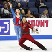 Marjorie Lajoie se tient debout, une main dans les airs et Zachary Lagha s'accroche à elle d'une main pour tourner autour.