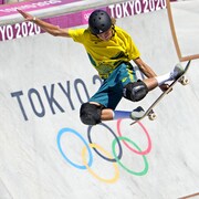 Dans un bol de compétition, devant le logo des Jeux olympiques de Tokyo, un spécialiste exécute un truc. 