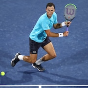 Le joueur de tennis tient sa raquette à deux mains et s'apprête à frapper la balle du revers. 