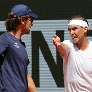 Deux hommes discutent sur un court de tennis.