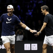 Un joueur de tennis sourit et félicite son partenaire de jeu en lui frappant la main durant un entraînement. 