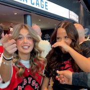 Deux jeunes femmes v&ecirc;tues de v&ecirc;tements &agrave; l'image des Raptors de Toronto r&eacute;agissent &agrave; une question avec des sourires. La femme &agrave; gauche pointe la cam&eacute;ra. Dans le coin inf&eacute;rieur gauche, on retrouve une image isol&eacute;e d'Ilrick Duhamel qui tient un ballon de basketball.